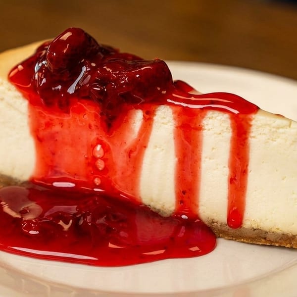 A slice of cheesecake with a graham cracker crust, topped with bright red cherry sauce.