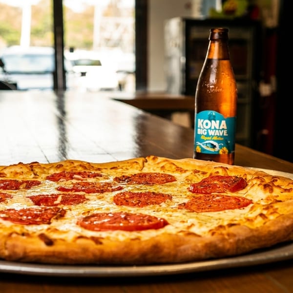 A whole pizza with tomato slices and cheese on a metal pan, with a beer bottle behind it.