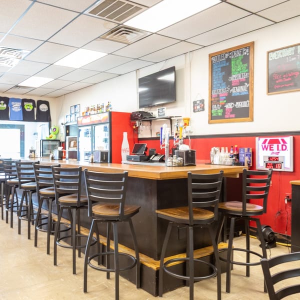 Interior view of a casual restaurant bar with stools, red walls, and menu chalkboards.