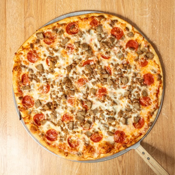 A large, round pizza with pepperoni and sausage on a wooden pizza peel.