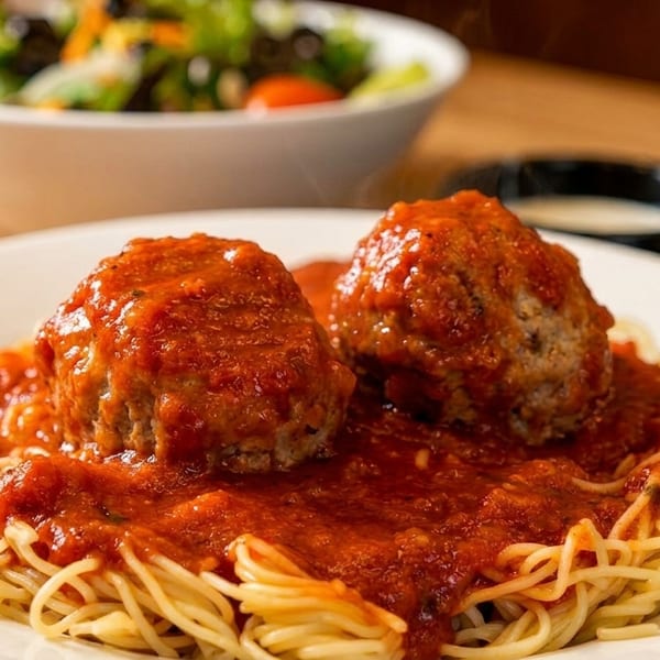 Spaghetti with two large meatballs and red sauce, with a salad in the background.