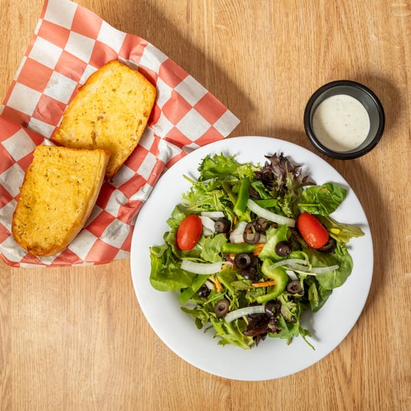 Fresh garden salad with tomatoes, olives, and onions, served with garlic bread and ranch dressing.
