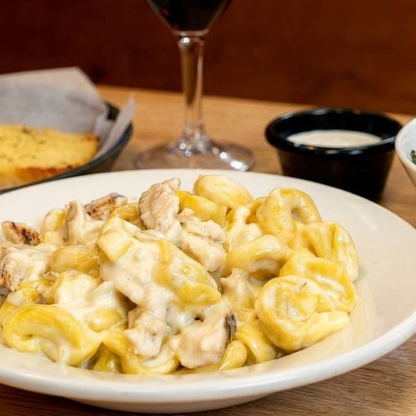 Chicken tortellini in cream sauce, with garlic bread, salad, and red wine on a wooden table.