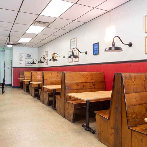 Empty restaurant dining room with wooden booths, red wainscoting, and black and white framed photos.