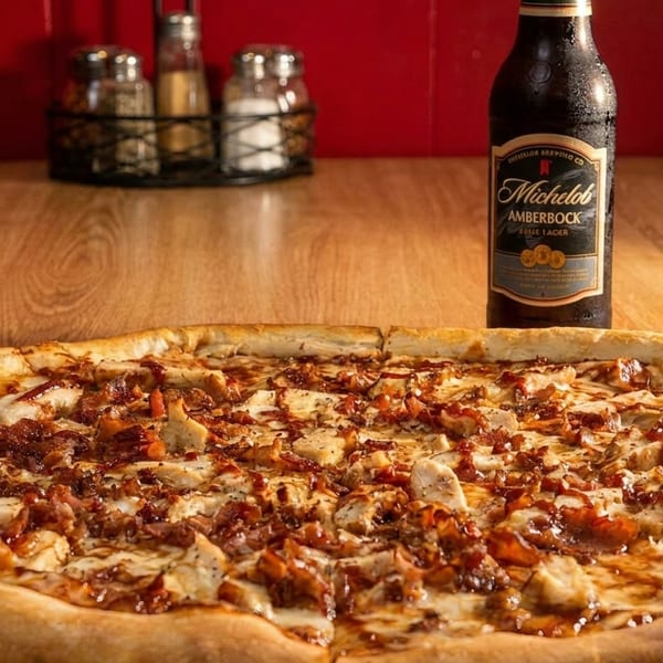 BBQ chicken pizza with bacon and a bottle of Michelob AmberBock beer on a wooden table.