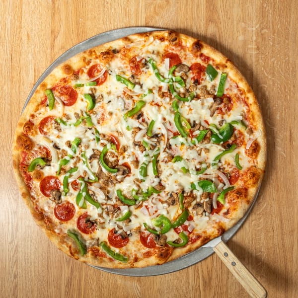 A whole supreme pizza with pepperoni, sausage, peppers, onions, and mushrooms on a wooden table.