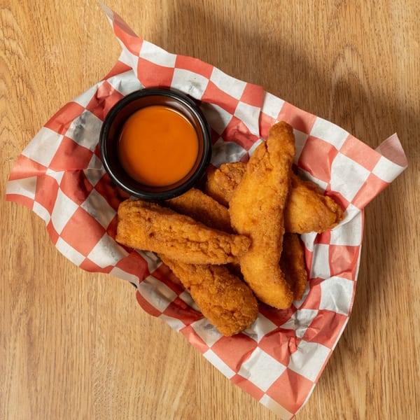 Crispy golden chicken tenders served in a red and white checkered paper with dipping sauce.