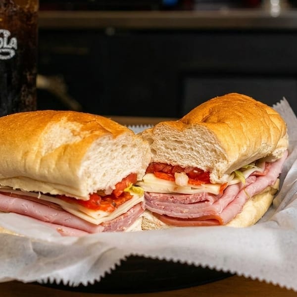 A large deli sub sandwich, cut in half, with a Pepsi-Cola drink in the background.