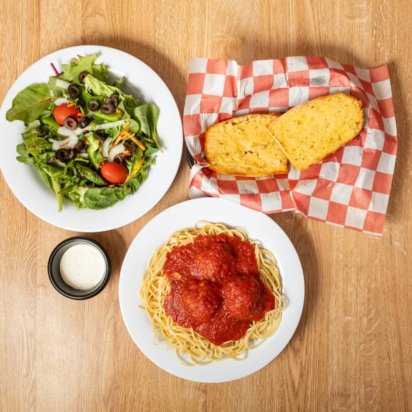 Spaghetti and meatballs, a side salad, and garlic bread on a wooden table.
