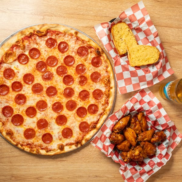 Pepperoni pizza, garlic bread, chicken wings, and a beer on a wooden table.