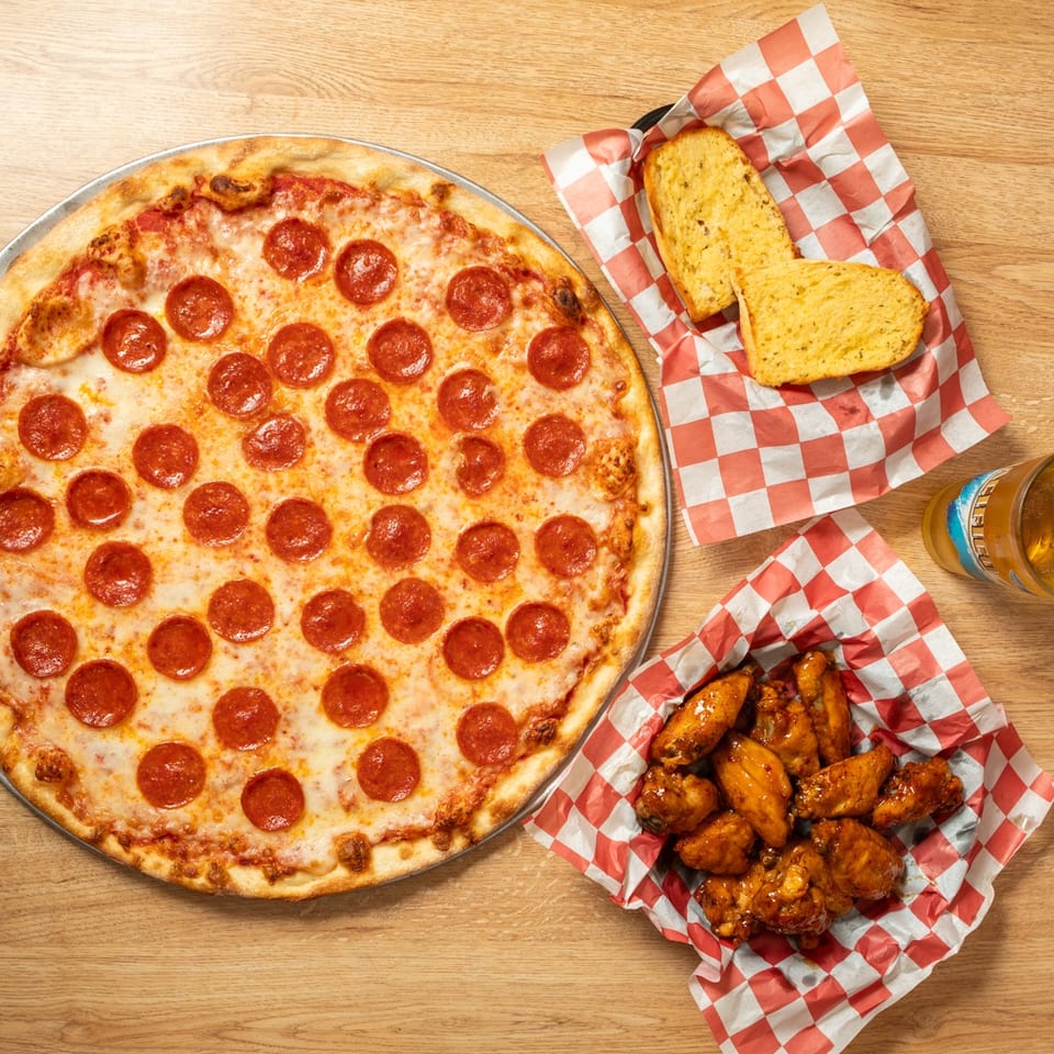 Pepperoni pizza, garlic bread, chicken wings, and a beer on a wooden table.