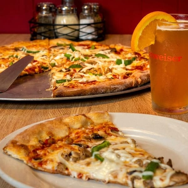 A whole pizza with a slice removed, next to a beer with an orange slice.