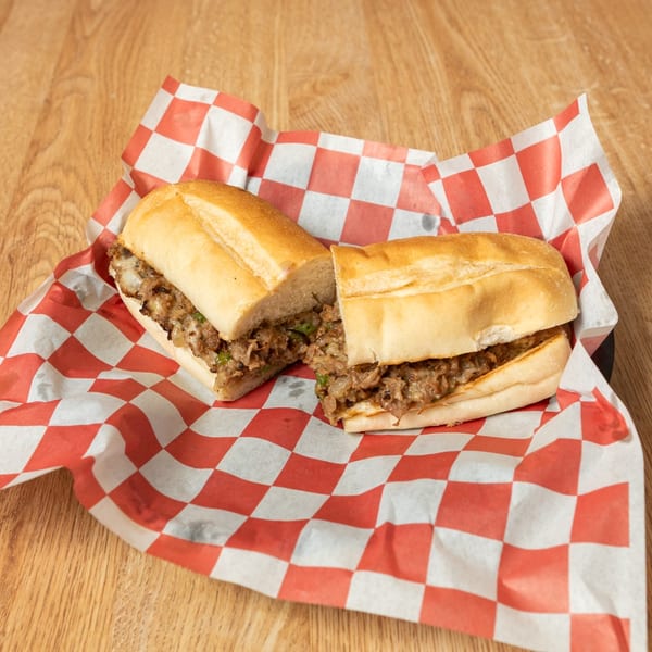 Cheesesteak sandwich cut in half, filled with meat, onions, and peppers on checkered paper.