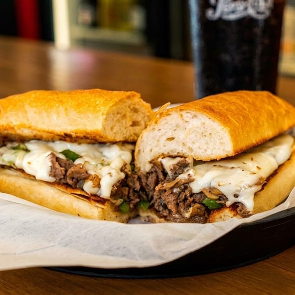 A delicious cheesesteak sandwich, cut in half, with melted cheese, steak, and green peppers.